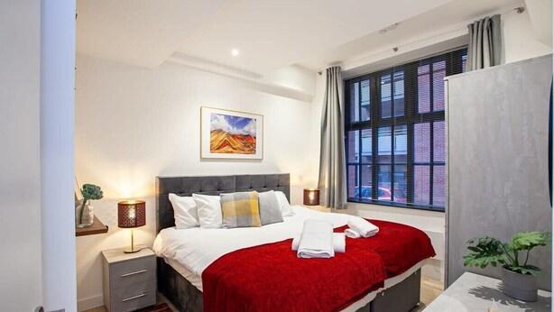 Une chambre d’hôtel moderne avec un grand lit, une table de chevet avec une lampe, une fenêtre avec des stores et un tableau au mur.
