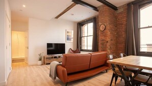 Een moderne woonkamer met een houten vloer, een bruine leren bank, een houten eettafel met stoelen, een flatscreen-tv en een bakstenen muur.