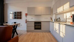 Een moderne keuken met witte kasten, een inbouwoven en een eethoek met een houten tafel en stoelen.