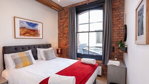 Een hotelkamer met een bed, een raam met gordijnen, een bakstenen muur en een schilderij aan de muur.