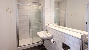 Een moderne badkamer met een glazen douchecabine, een witte wastafel en een grote spiegel.