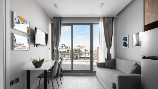 Eine moderne, gut beleuchtete Wohnung mit Essbereich, Sofa und großen Schiebeglastüren, die auf einen Balkon führen.