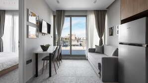 Ein modernes, helles Zimmer mit Essbereich, einer Couch und einem großen Fenster mit Blick auf die Stadt.