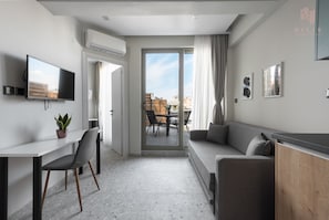 A modern living room with a sofa, a dining table, and a TV. - Skysphere Nilie Hospitality MGMT (Thessaloniki)