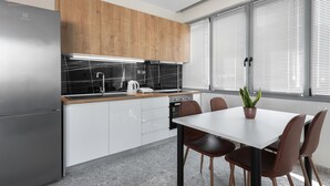 Eine moderne Küche mit einem Edelstahl-Kühlschrank, Holzschränken, einer schwarzen Arbeitsplatte und einem Essbereich mit einem weißen Tisch und braunen Stühlen.