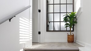 A staircase with a light wood finish, a white wall, a large window with a grid pattern, and a potted plant.