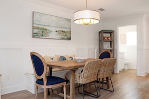 Uma sala de jantar com uma mesa de madeira, cadeiras de vime, um lustre e um quadro na parede.