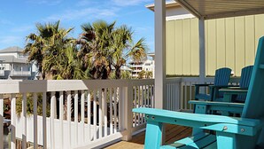 A balcony with a white railing, turquoise Adirondack chairs, and a view of palm trees and buildings.
