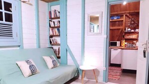 Une pi èce chaleureuse avec un canapé de couleur turquoise, une petite table blanche et un coin cuisine visible à travers une porte ouverte.