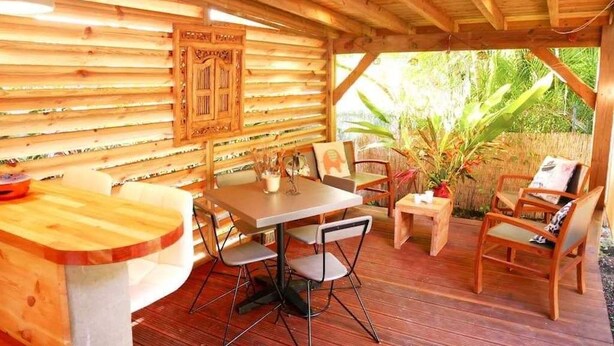 Une terrasse extérieure en bois, avec une table et des chaises, entourée d’une végétation luxuriante.