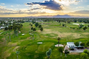 Vue aérienne d’un terrain de golf avec un club-house, des bunkers de sable et la végétation environnante.