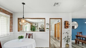 Un coin repas comprenant une table ronde, des chaises, un luminaire suspendu et une porte en bois donnant sur une autre pièce.