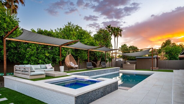 Un espace piscine extérieur moderne, doté d’un coin salon, d’un fauteuil suspendu et d’une terrasse couverte.