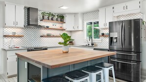 Une cuisine moderne avec des meubles blancs, un réfrigérateur en acier inoxydable, des plans de travail en bois et des tabourets de bar.