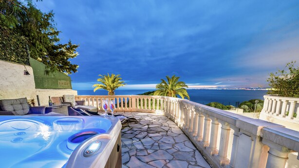 A stone-paved outdoor area with a hot tub, a white railing, and a view of the sea. - Amazing Villa Boron! View of the Sea, Pool, and Hot Tub (Nice)