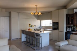 A modern kitchen with a central island, bar stools, a built-in oven, and a coffee machine. - Amazing Villa Boron! View of the Sea, Pool, and Hot Tub (Nice)