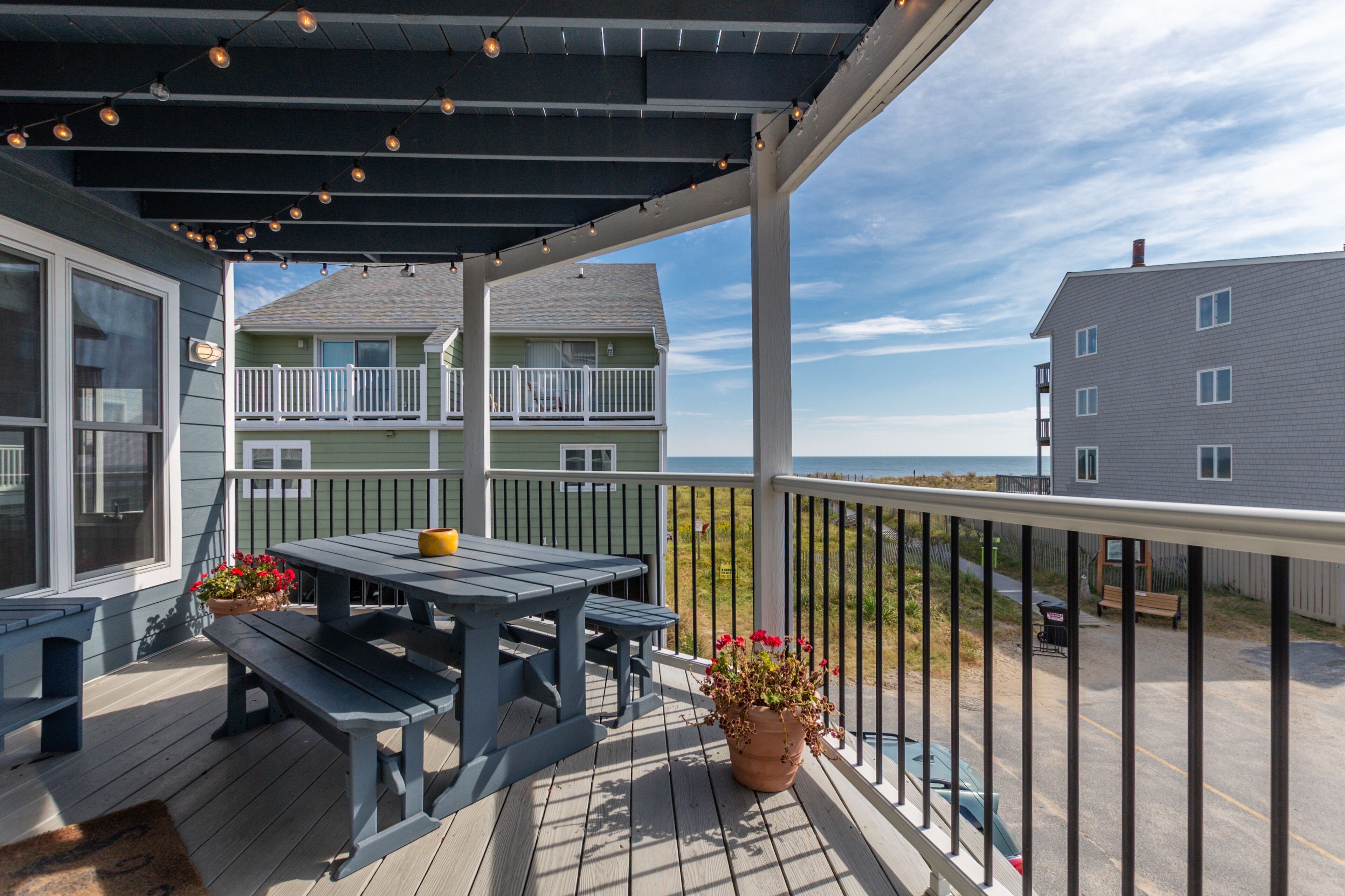 Um deck coberto com uma mesa e bancos, com vista para uma área residencial e o oceano.