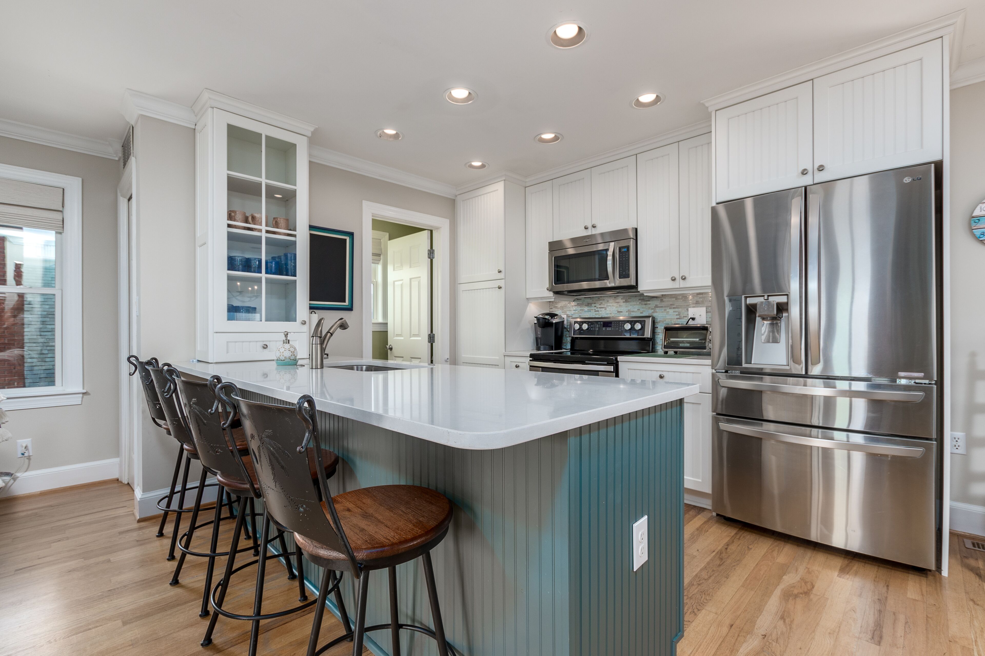 A modern kitchen with white cabinetry, stainless steel appliances, and a central island with bar stools.