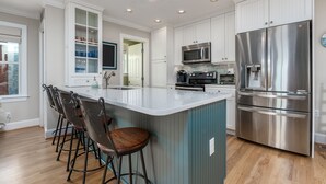 Une cuisine moderne avec des meubles blancs, des appareils en acier inoxydable et un îlot central doté de tabourets de bar.
