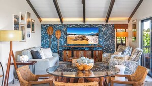 Una sala de estar con un televisor grande, muebles de mimbre y una pared con motivos tropicales.