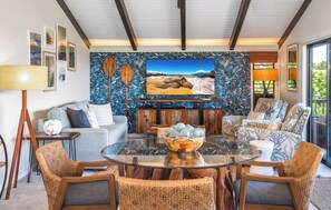 A living room with a large TV, wicker furniture, and a tropical-themed wall.