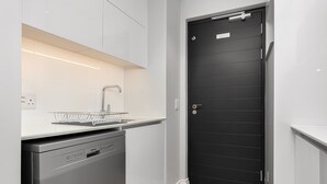 Une cuisine compacte équipée d’un lave-vaisselle, d’un évier avec un égouttoir en métal et d’une porte noire avec une plaque nominative.