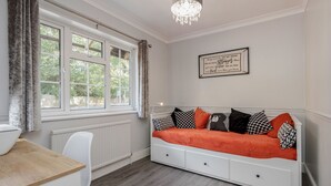 A room with a white sofa bed, a wooden table, a white chair, a window with curtains, and a chandelier. - Ascot Pet Friendly 4 Bed House Parking (Ascot)