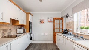 A modern kitchen with white cabinets, a microwave, a coffee maker, and a window with a view. - Ascot Pet Friendly 4 Bed House Parking (Ascot)