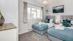 A modern bedroom with two beds, a large window with curtains, a chandelier, and a painting on the wall. - Ascot Pet Friendly 4 Bed House Parking (Ascot)