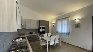 A modern kitchen with a dining area, stainless steel appliances, and a window with curtains. - Villa set just 100 meters from Sa Piscaiola Beach  (Porto Istana)
