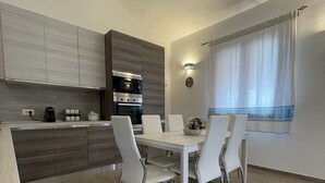 A modern kitchen with grey cabinets, a built-in oven, and a dining area with a white table and chairs. - Villa set just 100 meters from Sa Piscaiola Beach  (Porto Istana)