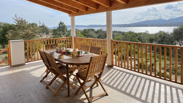 A wooden deck with a table and chairs, overlooking a scenic view of a lake and mountains. - Villa set just 100 meters from Sa Piscaiola Beach  (Porto Istana)
