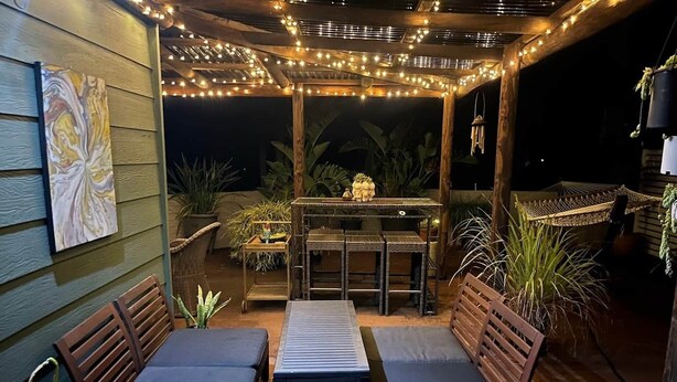 Une terrasse extérieure aménagée avec des meubles en bois, des guirlandes lumineuses et des plantes en pot.