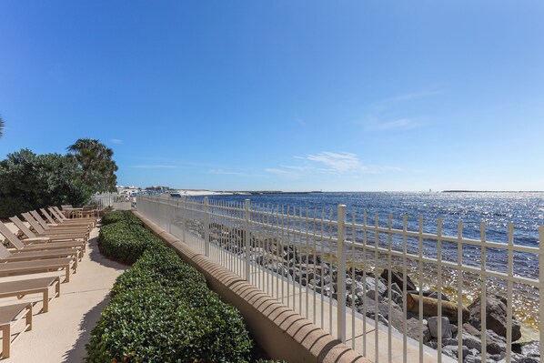 A seaside promenade with sun loungers and a white fence along the water's edge.