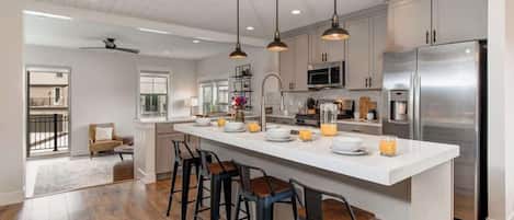 A modern kitchen with a central island, bar stools, stainless steel appliances, and pendant lighting.