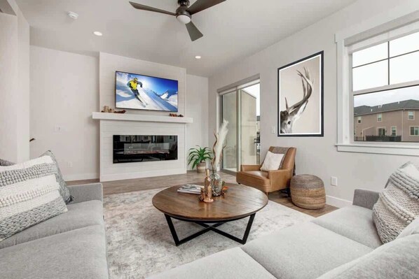 A modern living room with a fireplace, a round coffee table, and a television mounted above it.