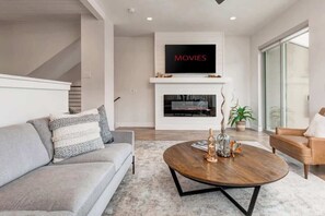 A modern living room with a sofa, coffee table, fireplace, TV, and a staircase.