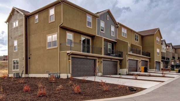 A multi-story residential building with a flat roof, multiple garage doors, and a landscaped front yard. - Alpine Adventure Haus! 4BR Townhome 15m to Main (Heber City)