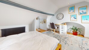 Een slaapkamer met een bed, een bureau, een stoel, een radiator, een klok en ingekaderde foto's aan de muur.