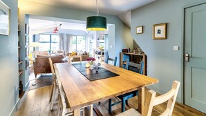 Un comedor amplio con mesa y bancos de madera, una cocina con armarios azules y vistas al exterior a través de grandes ventanas.
