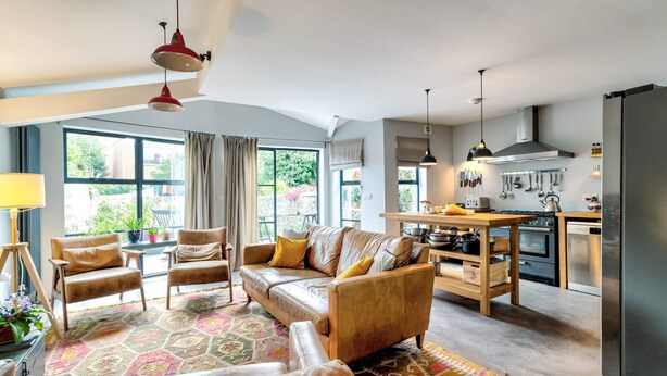Una sala de estar moderna con un sofá de cuero, una mesa de comedor y una zona de cocina con refrigerador y utensilios.