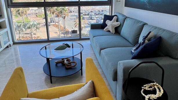 A modern living room with a large window, a sofa, a yellow armchair, a coffee table, and a black chair.