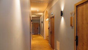 Un couloir doté d’un plancher en bois, de murs aux couleurs claires et d’une porte en bois située à droite.