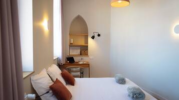 Une chambre à coucher avec un lit, des oreillers, un bureau avec un ordinateur portable, une chaise et une lampe.