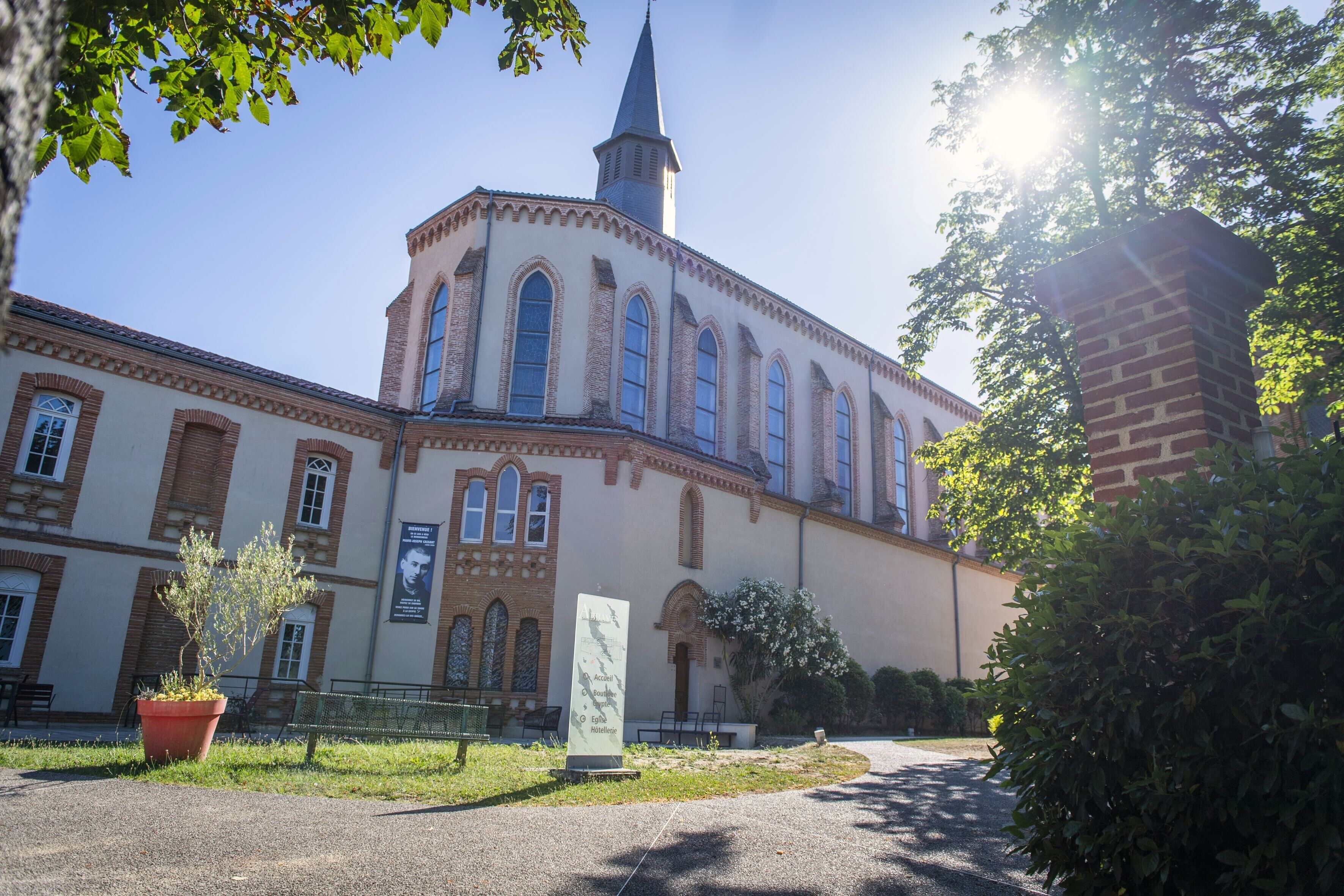 A historic building with a prominent tower and arched windows, surrounded by greenery and a paved walkway.