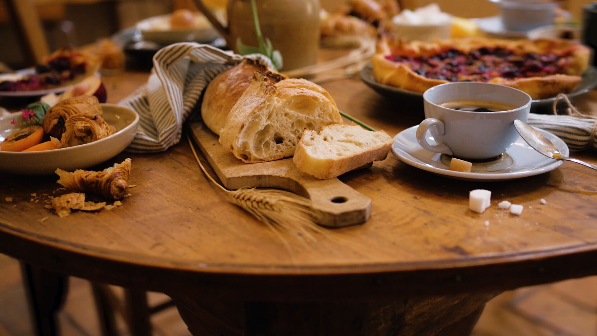 A wooden table with a variety of food items including bread, pastries, and a cup of coffee.