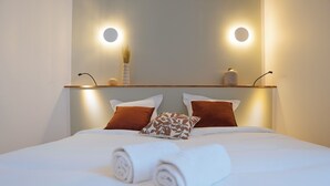 Un lit bien fait, avec du linge de lit blanc et des serviettes pliées, deux oreillers marron et un vase posé sur une table de chevet.
