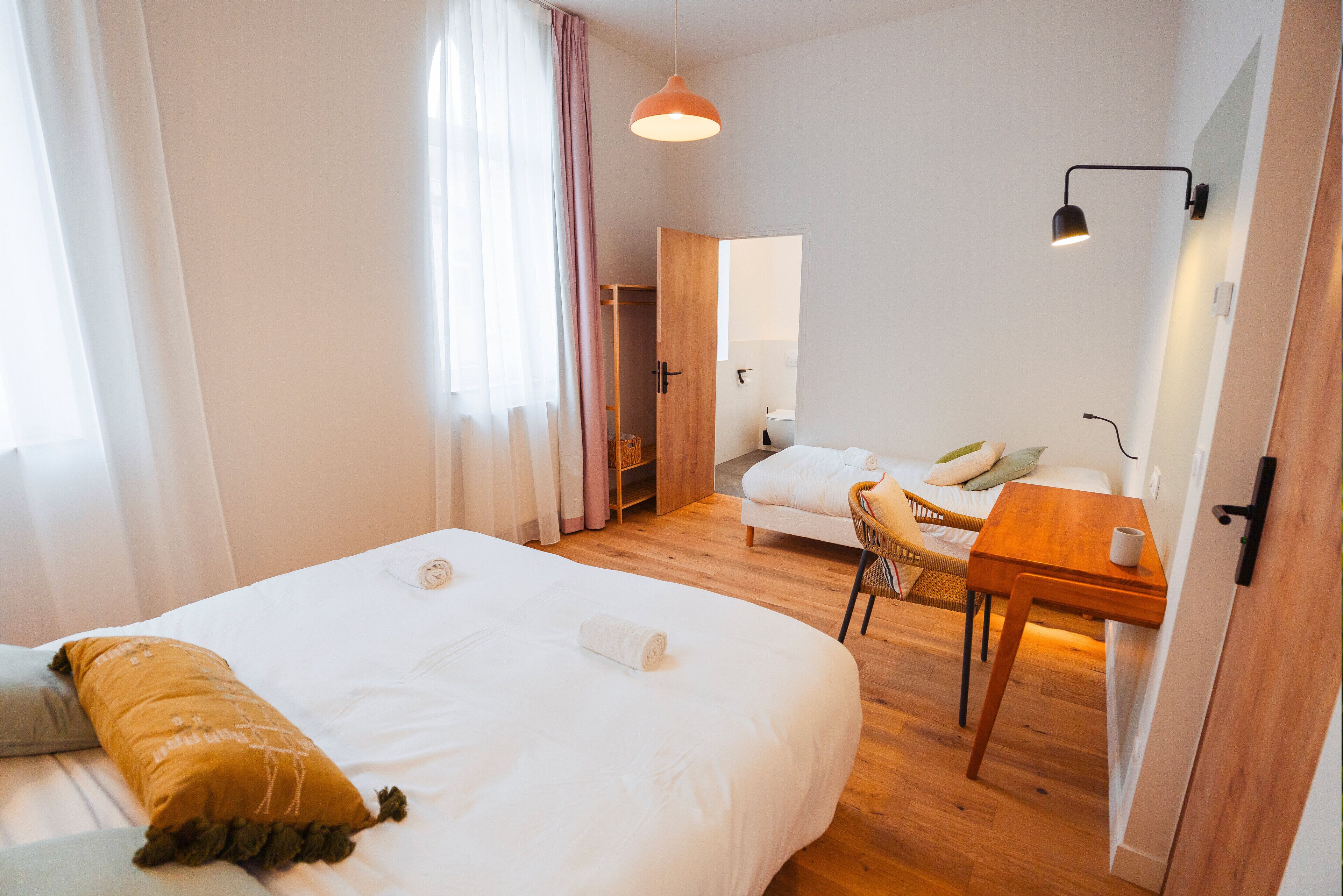 A hotel room with a large bed, a small desk, a chair, and a wooden floor.