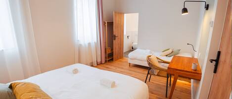 A hotel room with a large bed, a small desk, a chair, and a wooden floor.