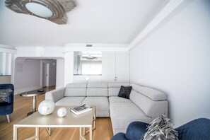 Een moderne woonkamer met een modulaire bank, een salontafel en een decoratieve spiegel aan het plafond.